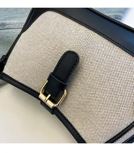Detail of canvas underarm bag featuring black leather trim and golden buckle closure