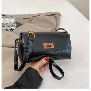 Detail of a chic black glossy leather crossbody bag with a gold metal turn-lock closure