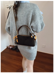 Detail of a matte black Boston bag with brown leather handles and vintage wooden beads