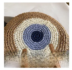 Detail view of woven round bag featuring a blue eye pattern and brown leather handle