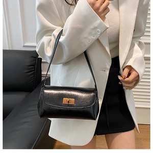 Close-up of black glossy leather shoulder bag with a rectangular gold metallic turn-lock buckle