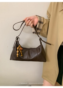 Détail d'un sac besace marron vintage avec des breloques en perles de bois sur la bandoulière