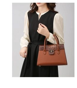 Detail of a brown leather tote with crocodile pattern flap and golden metal twist lock