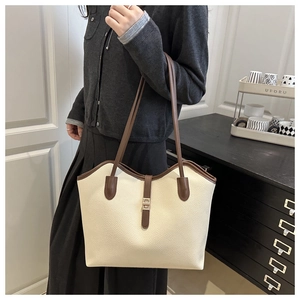 Detail of cream pebbled leather tote with brown straps and metal buckle on female model