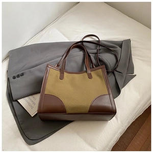 Detail of olive canvas tote bag with brown leather trim on soft fabric background