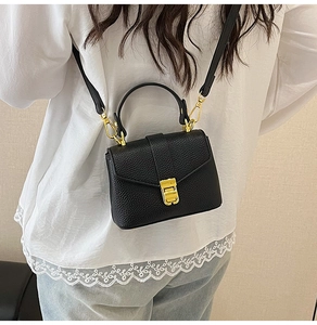 Detail of black lychee grain leather mini handbag with gold hardware and shoulder strap