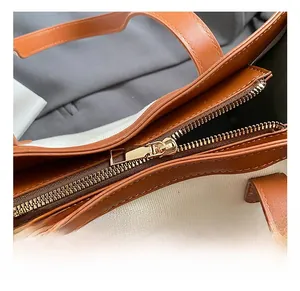 Close-up of golden metal zipper and brown leather trim on minimalist canvas tote bag