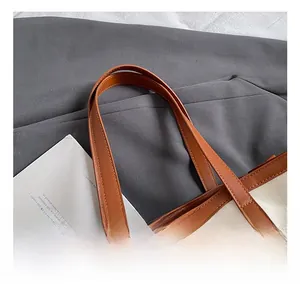 Close-up of canvas tote bag showing brown leather handles and meticulous stitching details