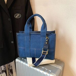 Large denim tote bag with contrast strap on silver suitcase in chic city travel setting