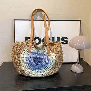 Handwoven round straw shoulder bag with evil eye pattern and leather handles