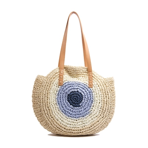 Round straw woven shoulder bag with blue evil eye pattern and brown leather straps