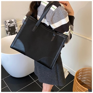 Minimalist black leather tote bag shown on model with reinforced handle stitching