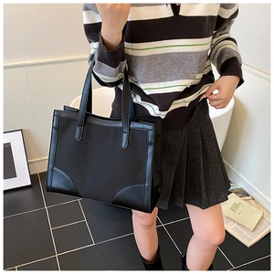 Side view of a large black canvas tote bag with leather trim on a model for daily commute