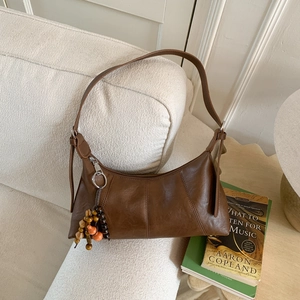 Sac à bandoulière vintage marron demi-lune avec breloque en perles sur canapé blanc