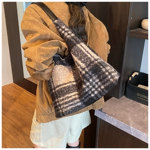 Detail of checkered plush tote bag with black leather strap on model in cozy interior
