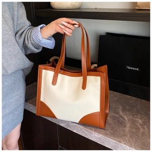 Detail of minimalist tote bag with off-white canvas and brown leather contrast stitching