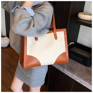 Detail of minimalist canvas tote bag featuring brown leather trim and stitching