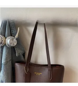 Detail of dark brown pebble leather tote bag with gold logo hanging on a wooden hook