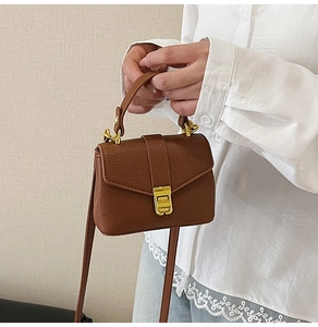 Close-up of brown litchi pattern leather handbag with gold metal lock and top handle
