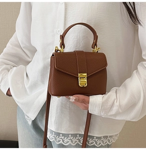 Detail of brown litchi grain leather shoulder bag with a gold clasp on a model