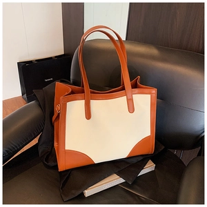 Close-up of orange and beige patchwork leather tote bag on a black leather chair