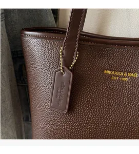 Close-up of dark brown lychee texture leather tote bag with gold lettering and brand tag