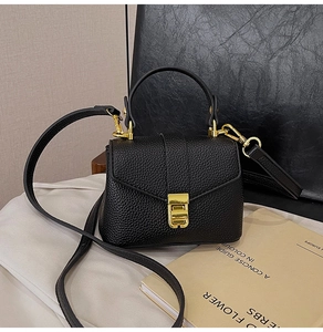 Detailed shot of a black litchi texture handbag with gold metal clasp and top handle