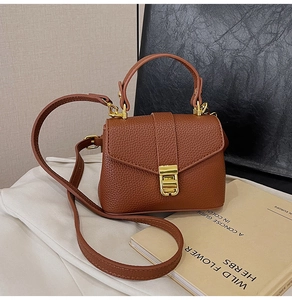 Detail of a brown lychee pattern leather handbag with golden lock on white fabric