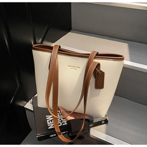 Detail of minimalist cream tote bag with litchi grain texture and gold brand logo