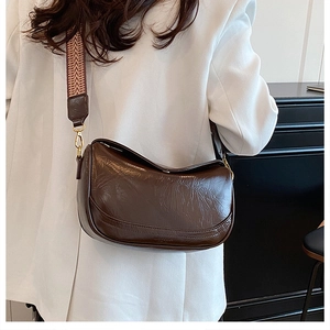 Detail of dark brown pleated crossbody bag with patterned strap and gold hardware