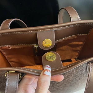Close-up of magnetic snap closure and zipper pocket inside brown leather tote bag