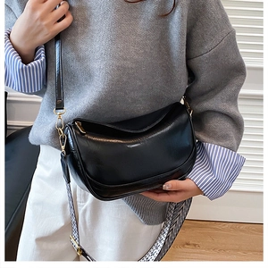 Close-up of black crescent bag with glossy texture and wide geometric strap detail