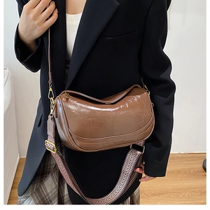 Detailed shot of brown glossy half-moon bag with patterned wide strap and fine leather strap