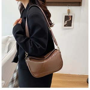 Detail of a brown half-moon bag featuring a geometric woven strap and matte leather texture