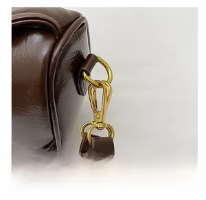 Detail showing the brown leather texture and golden metal lobster clasp of the bag