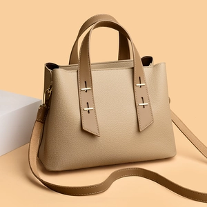 Detail of cross-shaped gold buckles and adjustable strap on beige leather tote bag