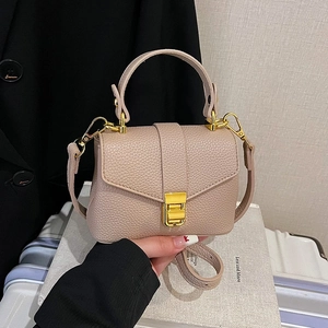 Elegant beige lychee grain leather handbag with gold buckle shown in a stylish travel scene