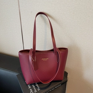 Elegant burgundy leather tote bag with gold logo and litchi texture on a book background