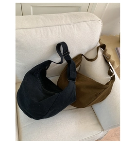 Close-up of black and coffee canvas half-moon bags with adjustable straps on a soft sofa