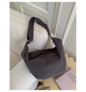 Detail of dark grey canvas hobo bag with wide adjustable strap on a white sofa