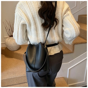 Detail of black pebbled leather bucket bag with adjustable strap worn as a shoulder bag