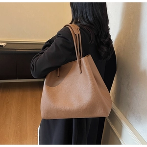 Detail view of warm brown leather tote bag with lychee texture worn by a model