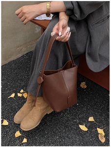 Detail of dark brown pebble leather bucket bag with fine stitching in a fall outdoor setting
