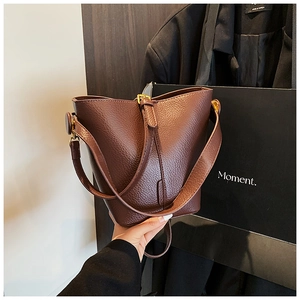 Detailed macro view of deep brown litchi grain leather bucket bag with golden buckle