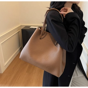 Detail of a large brown pebbled leather tote bag worn on shoulder in a minimalist room