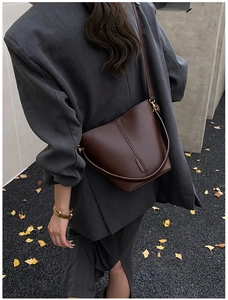 Detail of dark brown pebble leather bucket bag with vertical stitching and dual straps