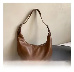 Détail de la texture en cuir souple et couture du sac hobo marron sur fond minimaliste