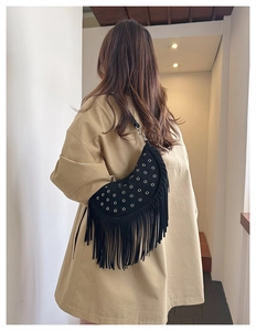 Detail of a black suede crescent bag featuring long fringe and silver metal eyelets