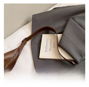 Détail d'un sac cabas en cuir marron avec large bandoulière sur un costume gris