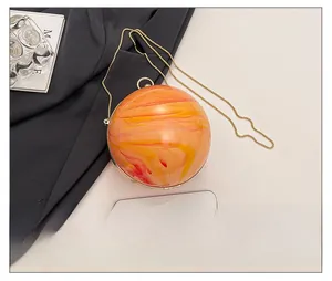 Sac boule en acrylique marbré orange avec chaîne dorée à côté d'un smartphone de taille